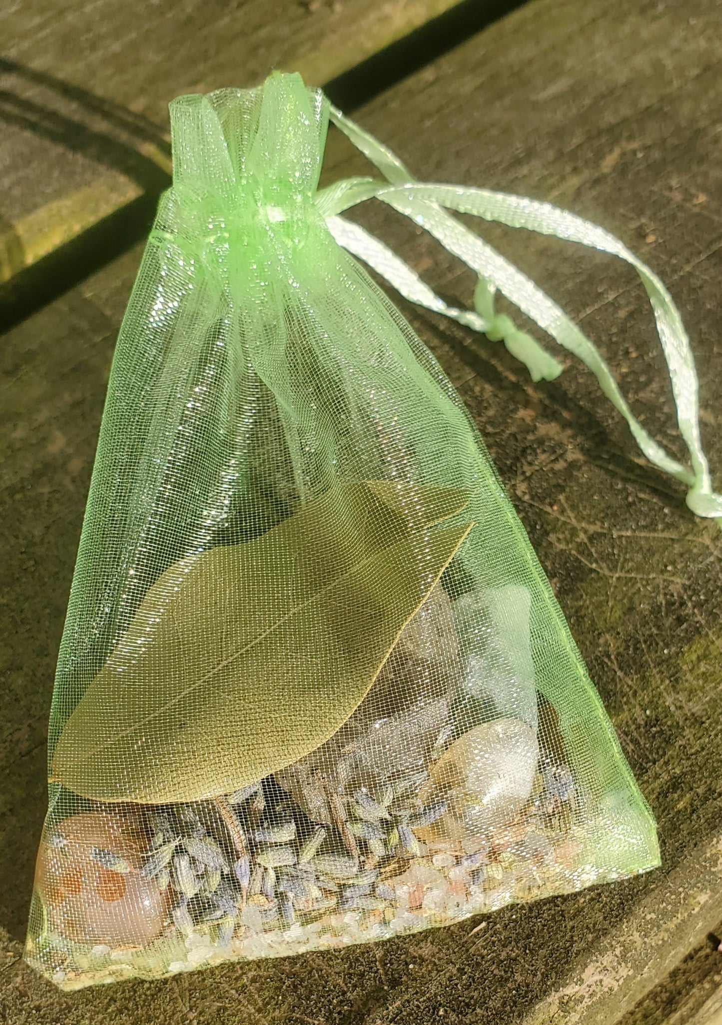 A green organza bag with light green strings filled with crystals and herbs.