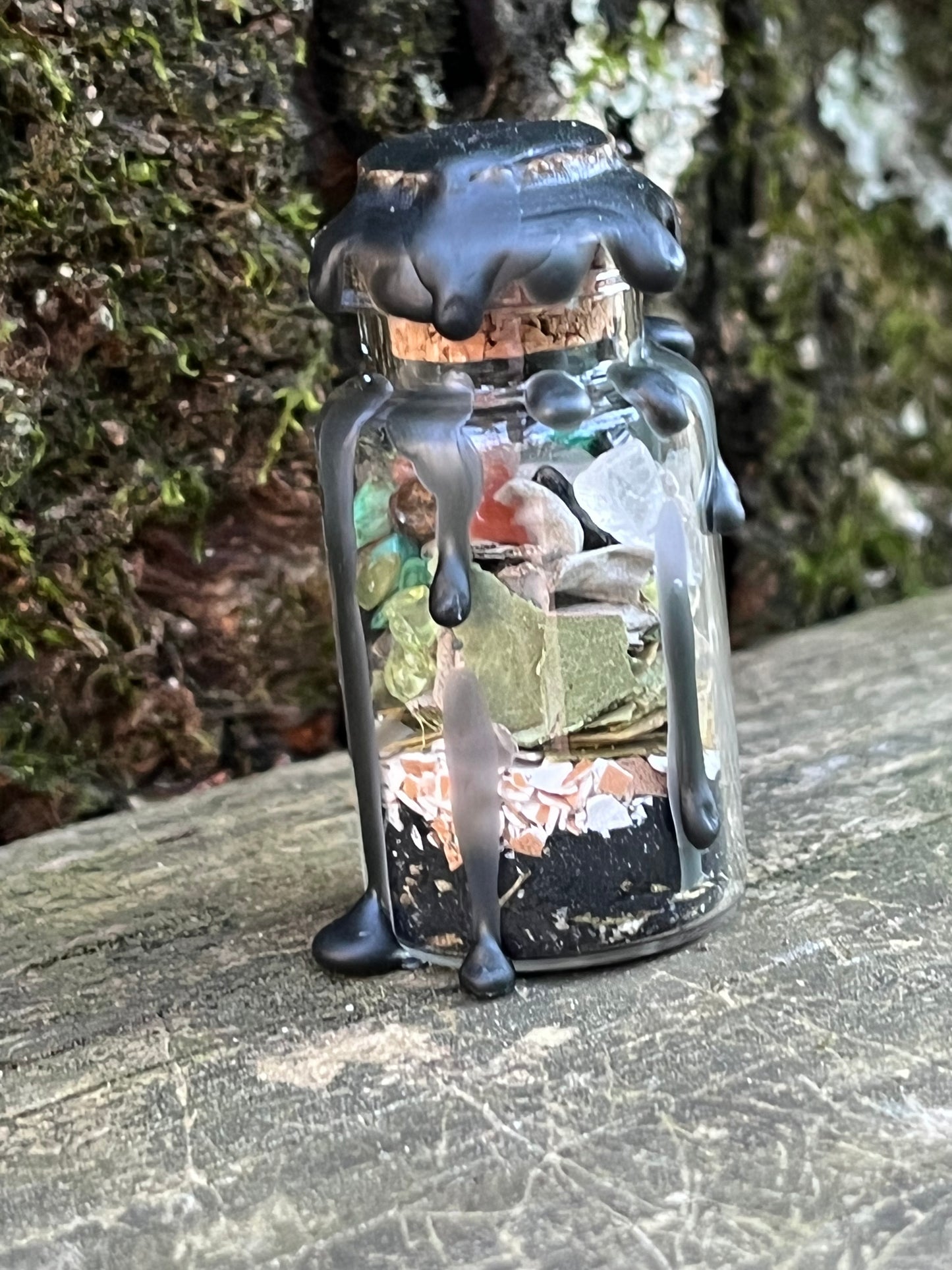 A glass bottle filled with herbs, crystals, and powders sealed with black wax.