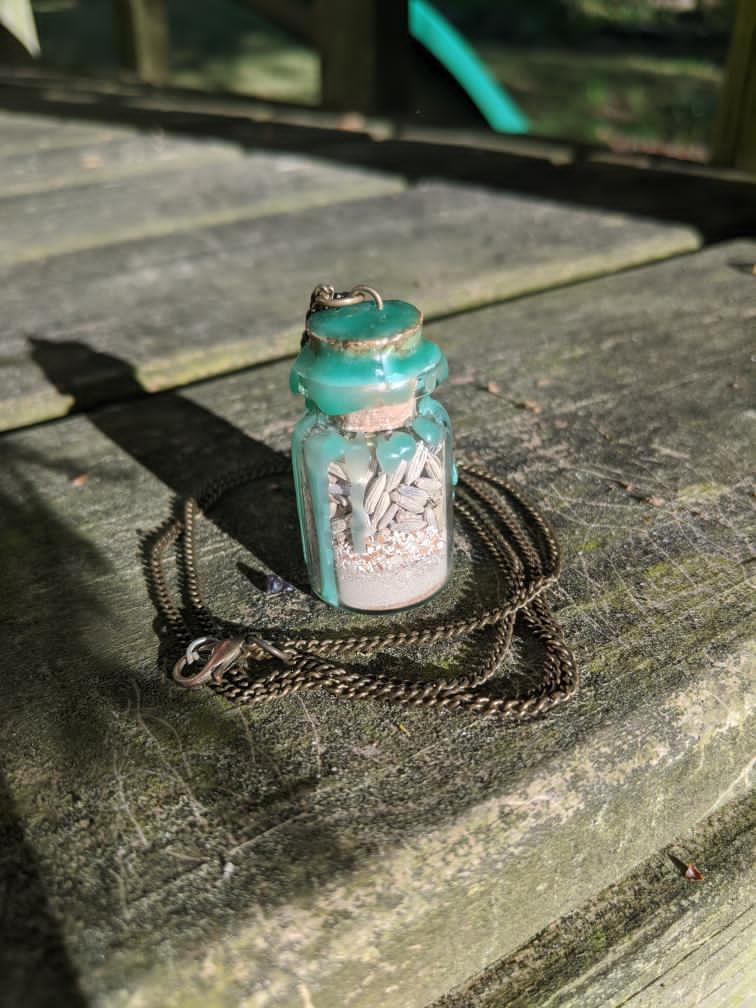 A glass bottle filled with herbs, crystals, and powders, sealed with green wax and on a chain.
