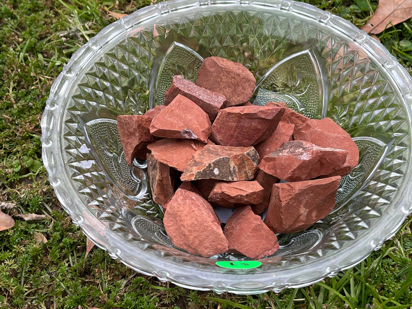 Chunks of raw red jasper in a round glass bowl. The bowl is set on the grass.