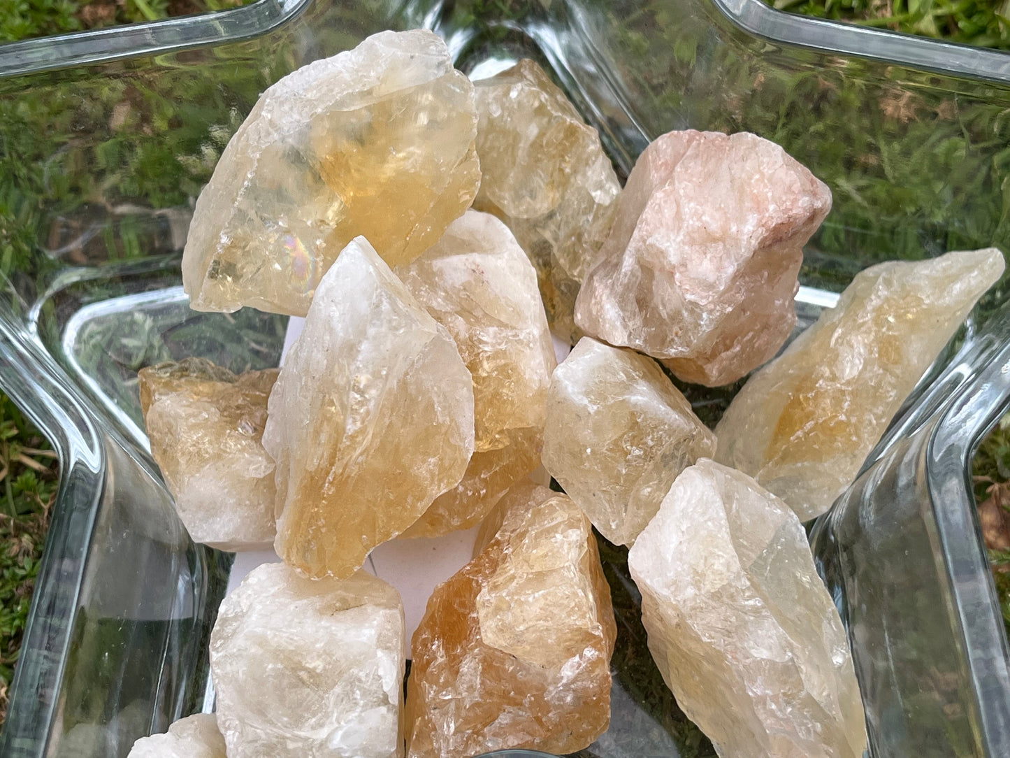 Pieces of raw citrine in a star-shaped, glass bowl. The bowl is in the grass.