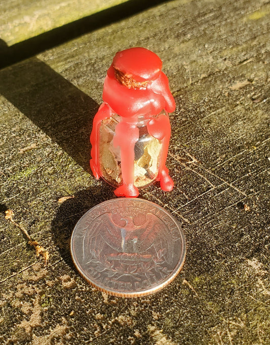 A glass bottle filled with herbs, crystals, and powders, sealed with red wax. There is a quarter laying next to the bottle.