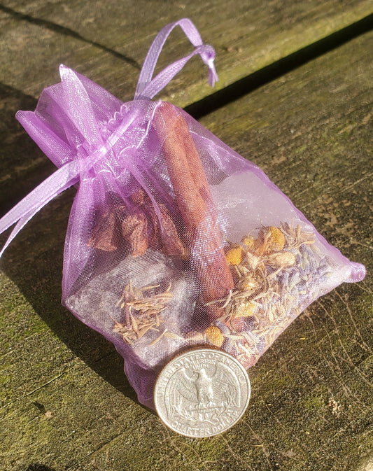 A purple organza bag with purple strings filled with crystals and herbs. There is a quarter laying on part of the bag.