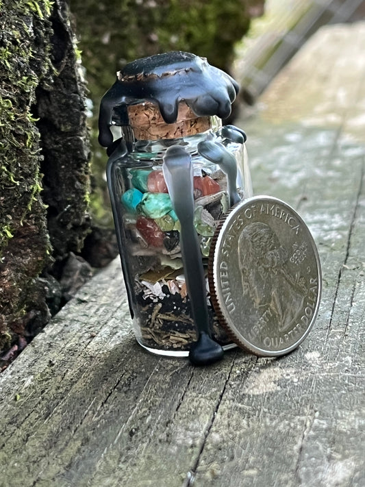 A glass bottle filled with herbs, crystals, and powders sealed with black wax. There is a quarter leaning against part of the bottle.