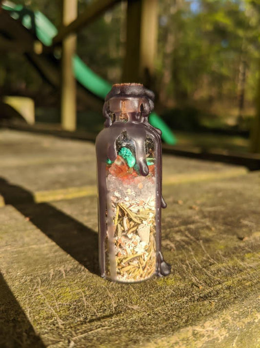 A glass bottle filled with herbs, crystals, and powders sealed with black wax.