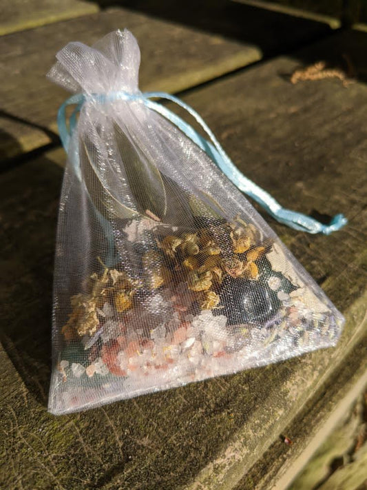 White organza bag with blue strings, filled with herbs and crystals.