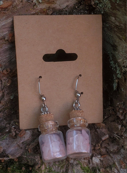 Two glass bottle earrings filled with rose quartz chips and put in a brown card backing.