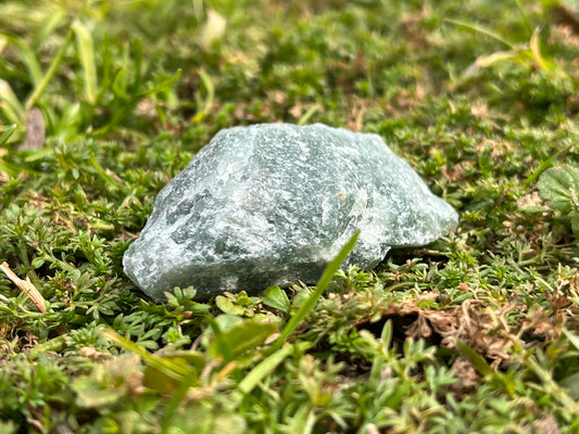 A piece of raw green aventurine in a patch of moss.