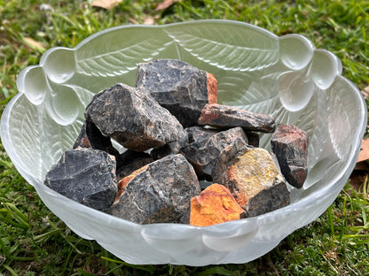 Chunks of raw black onyx in a round, frosted, glass bowl. The bowl in set in the grass.